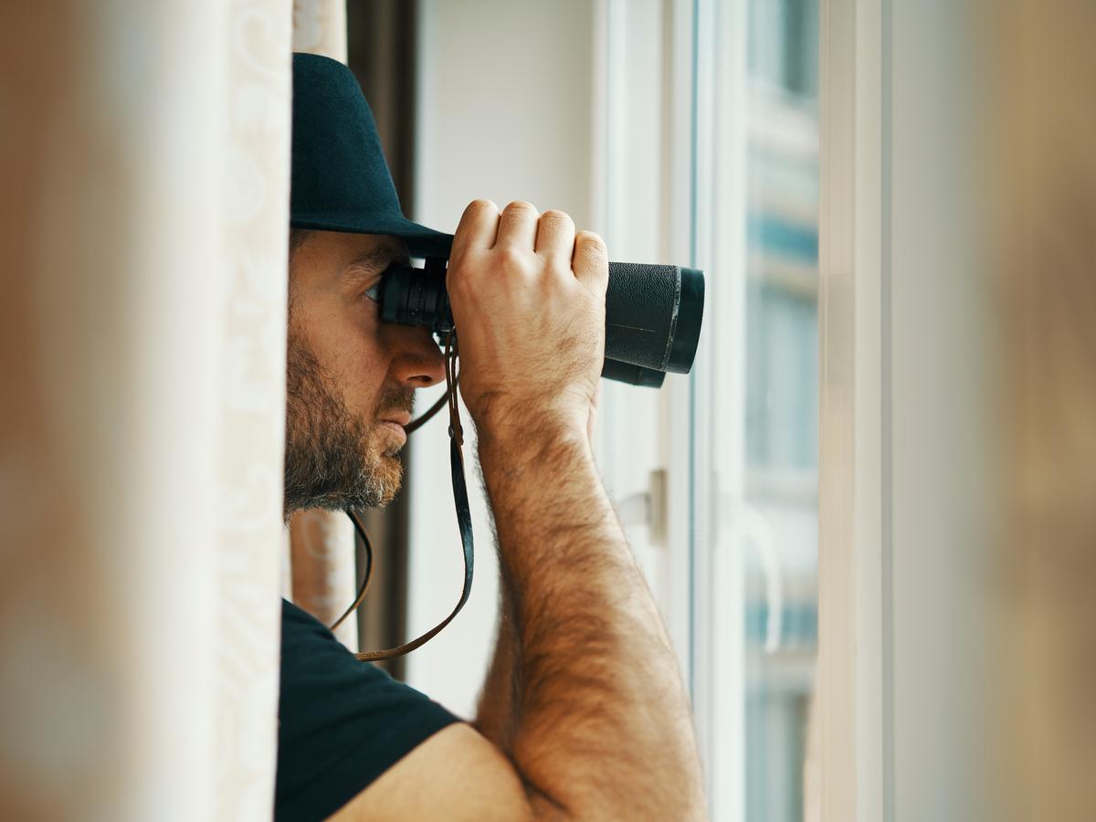 Private investigator watching through binoculars from an indoor window