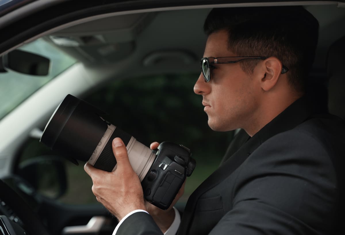 Investigator in a vehicle documenting activity with a camera